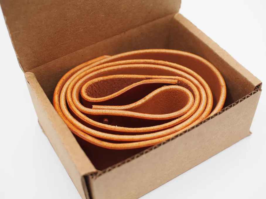 a pair of chestnut straps coils around itself in a small cardboard box, ready to ship