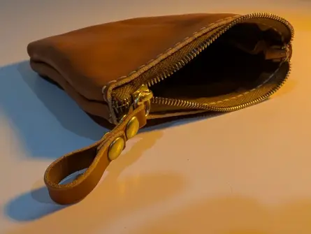 a small tan zipper pouch, with bright brass rivets on its pull tab